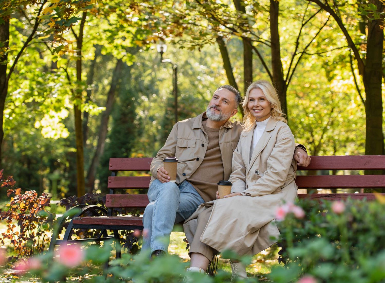 Mission 106 Luxury Apartments happy, loving mature couple holding coffee to go while spending time sitting on a bench in a lush green park